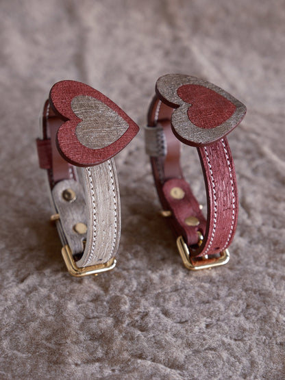 Two leather dog collars with heart designs on a textured surface.